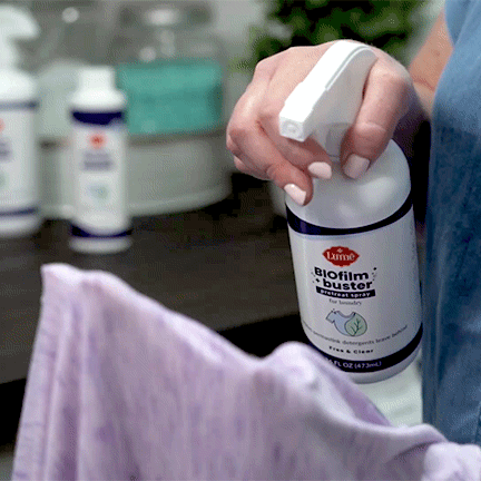 Woman-applying-Lume-pre-laundry-spray-to-a-purple-shirt-with-a-counter-with-several-Lume-laundry-products-in-the-background.gif